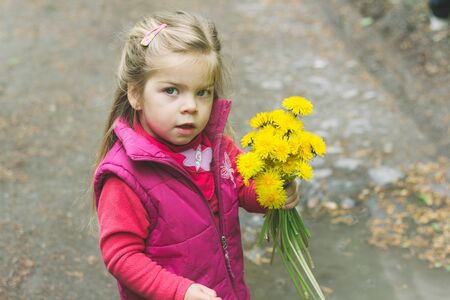 Little baby girl holding flowers on a natural mountain background in the spring season