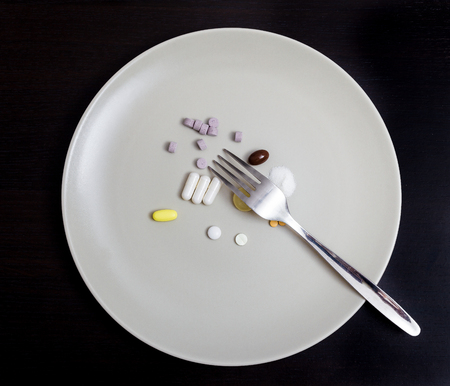Several pills of different shape and color on a grey plate along with a forkの写真素材