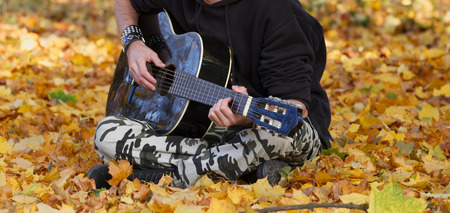 Young man playing guitar in the middle of the nature during the fall season, artistic conceptの写真素材