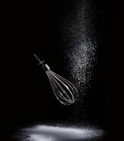 Shiny stainless eggbeater and pouring flour isolated on black backgroundの写真素材