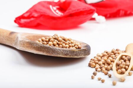 Aromatic color coriander seeds ingredient on white table with wooden rustic scoop and red fabric bag in backgroundの写真素材