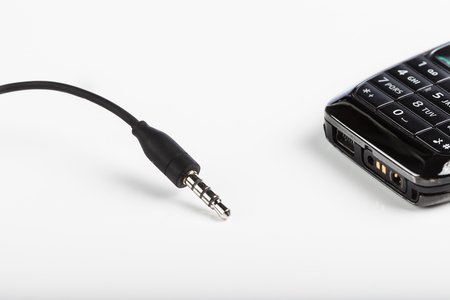Mobile cellphone accessories, plug, earphones, connectors isolated on a white background with a black telephone with keyboardの写真素材