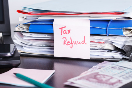 Handwritten note with tax return, refund text, formas and papers, notebook and laptop with mobile phone, cash on the tableの写真素材