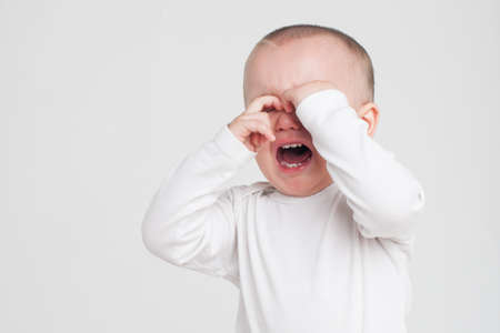 baby on a white background crying in a white pajamas