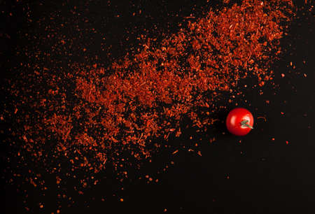 fresh tomato with crumbled red pepper closeup on a black backgroundの写真素材
