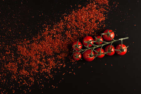 fresh tomatoes on a branch with crumbled red pepper closeup on a black backgroundの写真素材