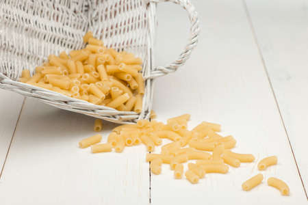 pasta in wicker basket and scattered on a white old wooden boardsの写真素材