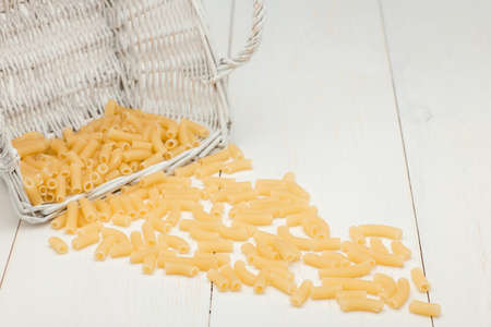 pasta in wicker basket and scattered on a white old wooden boardsの写真素材