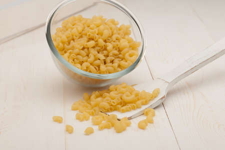 pasta in a transparent plate of glass and wooden spoon on a white old wooden boardsの写真素材