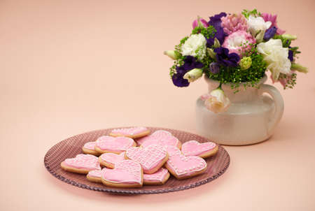 pink cookies in the shape of hearts on a plate and flowers on Valentine's Dayの写真素材
