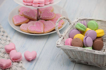 pink cookies in the shape of hearts on a plate and pastries in a wicker basket on the wooden boards on the day of valentineの写真素材