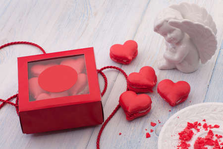 Red cookies in the shape of a heart in a gift box on wooden boards and a plate and decorated with...