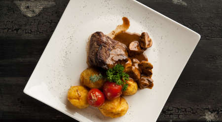 meat dish on a wooden old surface. fried meat with potatoes in a white plate on a wooden old boardの写真素材