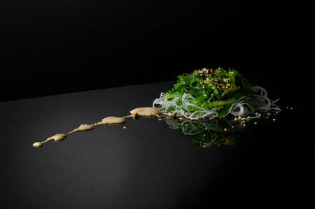 seaweed and onion with sesame seeds on a black background with reflection. a bundle of seaweed with onions on a dark surface with reflectionの写真素材
