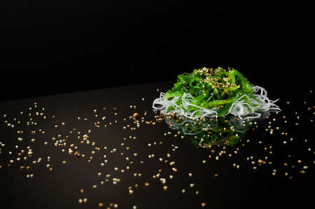 seaweed and onion with sesame seeds on a black background with reflection. a bundle of seaweed with onions on a dark surface with reflectionの写真素材