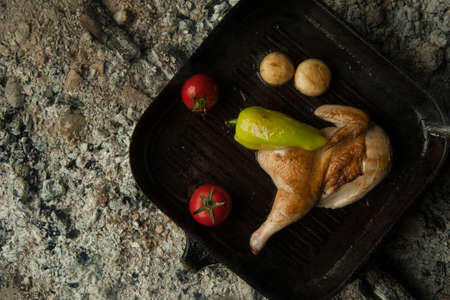 chicken meat with tomatoes on a baking sheet lie on charcoal. the dish is cooked and smoked on charcoalの写真素材