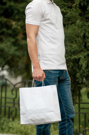 man with a white paper bag in hands on a park background. courier with a bag on the background of a green parkの写真素材