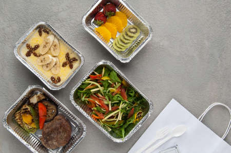 fast food in a foil box on a gray background. a healthy food close up. delivery from the restaurant a set of healthy foodの写真素材