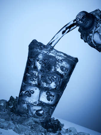 pouring  water from a plastic bottle into a glass with ice on a light blue background
