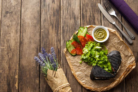 sandwich of black bread with vegetables on a wooden surfaceの写真素材