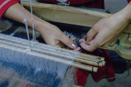 weaving and manufacturing of handmade fabric close up. women's hands behind a loom make clothの写真素材