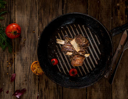 fried meat with bone in the pan on wooden background, top viewの写真素材