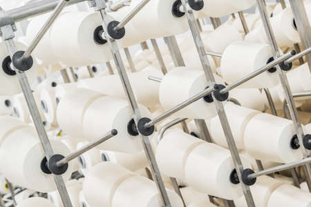 Coils of white cotton threads on metal racks. close up