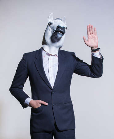 A man in a suit and a horse mask on a light background. Conceptual business backgroundの写真素材