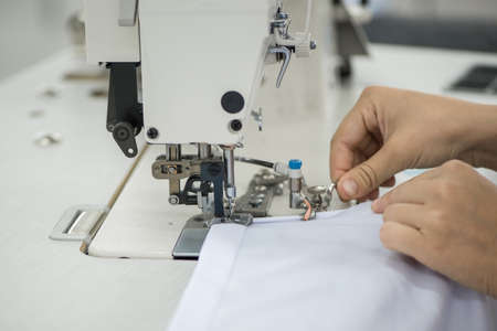 seamstress on a sewing machine makes a shirt in the sewing workshop. the woman on the machine sews...