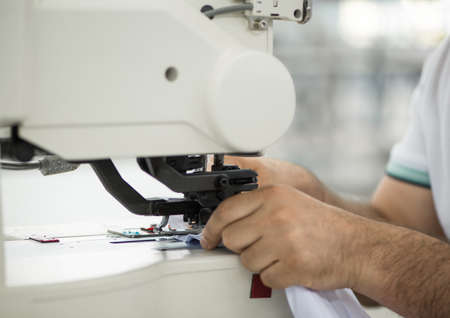 seamstress male on a sewing machine makes a shirt in the sewing workshop. the man on the machine sews the collar and cuffsの写真素材