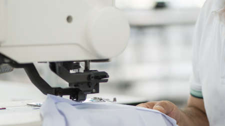 seamstress male on a sewing machine makes a shirt in the sewing workshop. the man on the machine...