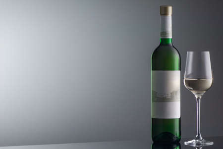 bottle of white wine with wineglass on grey background with illuminationの写真素材