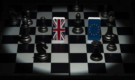Backlit in the shadows figures and flags of the European Union and Great Britain on the chessboard....