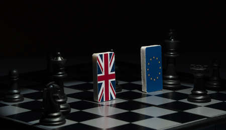 Backlit in the shadows figures and flags of the European Union and Great Britain on the chessboard....