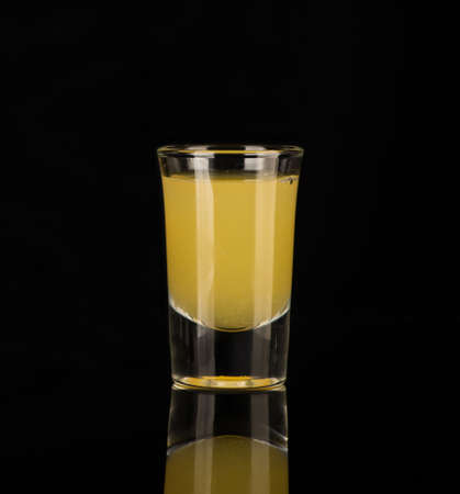 yellow alcoholic liquor in a shot glass isolated on dark backgroundの写真素材