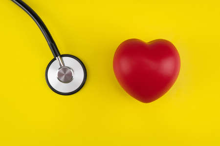 Toy heart and a stethoscope on a yellow background. Top view. Concept healthcare. Cardiology - care of the heartの写真素材