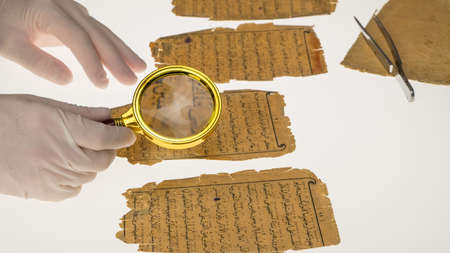 A researcher studies Arabic writing from the Koran using a magnifying glass and a table with a light. Paleography, the study of ancient Arabic writingの写真素材