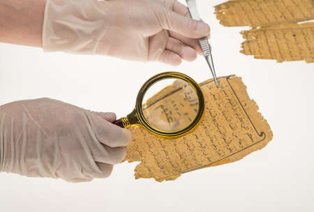 A researcher studies Arabic writing from the Koran using a magnifying glass and a table with a...