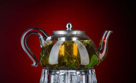 Tea with mint and herbs in a transparent teapot on a red background. Isolated with backlightの写真素材