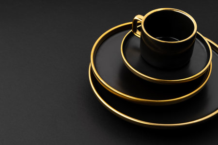 A set of black and golden ceramic plates and cups on a black backgroundの写真素材