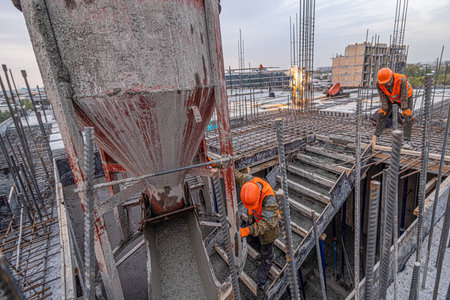 The workers on a building infrastructure roof with machinery and tools. Pouring concrete into a moldの写真素材