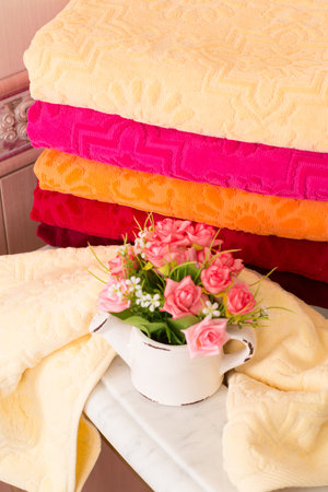 A vertical shot of folded colorful bamboo towels on a bathroom cabinet with a bouquet decorationの写真素材