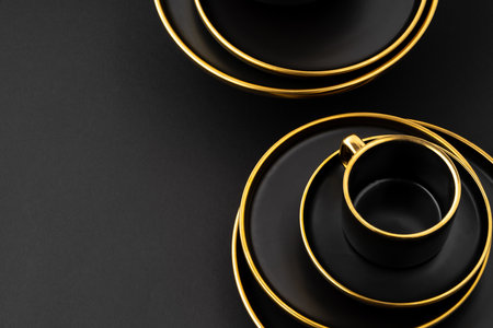 A set of black and golden ceramic plates and cups on a black backgroundの写真素材