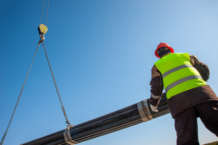 A low-angle shot of a person standing trying to carry industrial pipes on a craneの写真素材