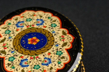 A closeup of a round casket with an artistic painting on a black background. Central Asia,...