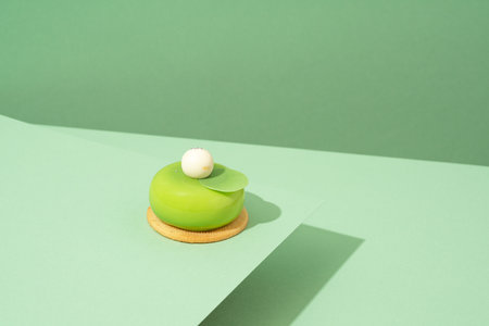 A freshly baked pastry with green and white icing, sitting atop a green-hued surfaceの写真素材