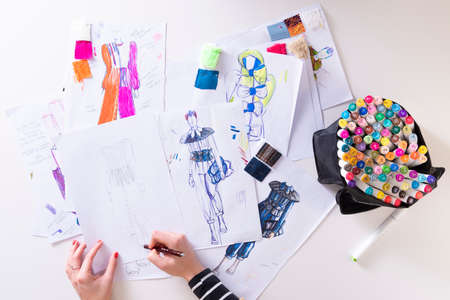 young brunette woman designing fashion dresses drawing with colored pencils. Various colorful fashion drawings and sketchの写真素材