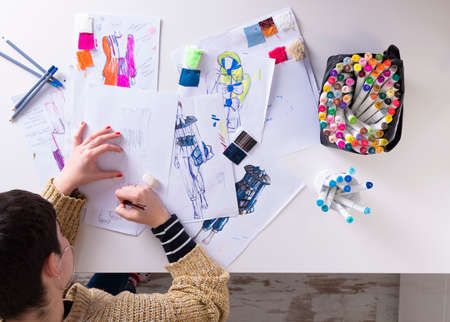 young brunette woman designing fashion dresses drawing with colored pencils. Various colorful fashion drawings and sketchの写真素材