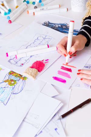 young brunette woman designing fashion dresses drawing with colored pencils. Various colorful fashion drawings and sketchの写真素材