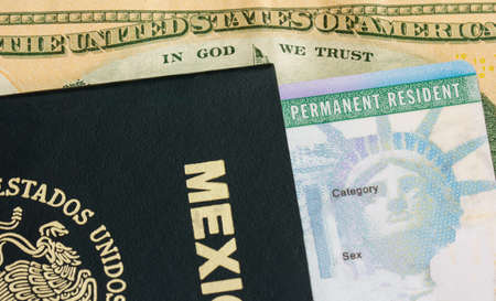 Permanent resident card  green card  with a mexican passport over a dollar billの写真素材